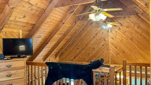 A wooden interior with a sloped ceiling, a ceiling fan, a television, and a plush toy. - Sitting Rock - Cabin In The Smokies (Sevierville)