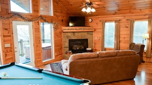 A cozy cabin interior with a pool table, a fireplace, a sofa, and a television. - Unforgettable - Cabin (Sevierville)