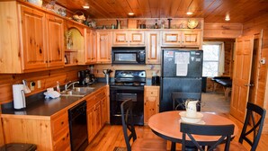 A wooden cabin kitchen with wooden cabinets, a microwave, stove, refrigerator, and a dining table with chairs. - Unforgettable - Cabin (Sevierville)