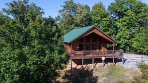 A wooden cabin with a green roof, a balcony, and surrounded by dense trees. - Unforgettable - Cabin (Sevierville)