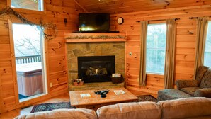 A cozy cabin interior with a stone fireplace, a television, and a comfortable seating area. - Unforgettable - Cabin (Sevierville)