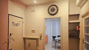 Un pasillo con un radiador, una puerta con la etiqueta 'Queen', un reloj y una escalera que conduce a otra habitación.