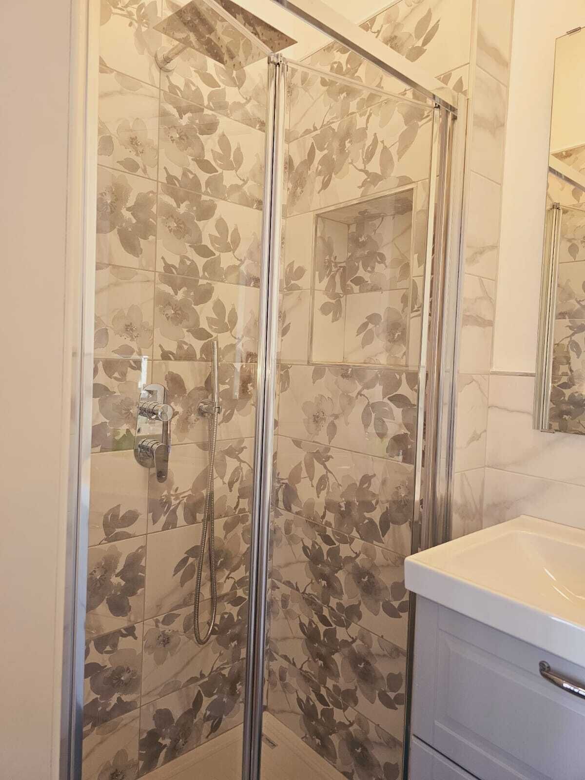 Eine Dusche mit Glastür, ein weißes Waschbecken und ein Spiegel darüber.