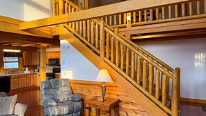 A wooden staircase with a lamp on the landing, a cushioned chair, and a kitchen area with wooden cabinets and appliances. - Harvest Moon - Cabin In The Smokies (Sevierville)