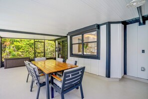 Un espace repas avec une table et des chaises en bois, de grandes fenêtres et une vue sur la verdure.
