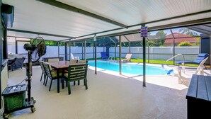 Ett takförsett utomhusområde med en pool, solstolar och ett bord med stolar.
