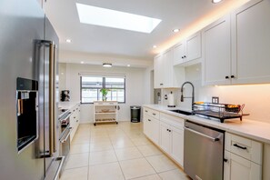 A modern kitchen with white cabinetry, a stainless steel refrigerator, a dishwasher, and a window providing natural light. - Renovated Naples Oasis w/ Pool: 2 Mi to Beach (Naples)