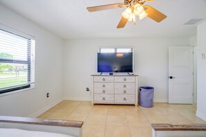 A bedroom with a ceiling fan, a television on a dresser, a window with blinds, a door, and a trash can. - Renovated Naples Oasis w/ Pool: 2 Mi to Beach (Naples)