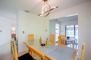 A dining area with a glass-top table, wooden chairs, and a modern chandelier. - Renovated Naples Oasis w/ Pool: 2 Mi to Beach (Naples)