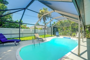 A swimming pool with a clear blue water, surrounded by a covered area with lounge chairs and a white fence.