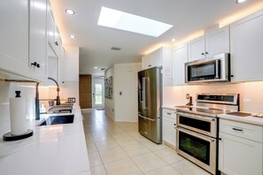 A modern kitchen with white cabinetry, stainless steel appliances, and a skylight.