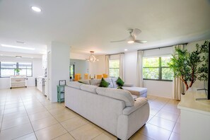 A modern living room with a sofa, a dining area, and a kitchen in the background.