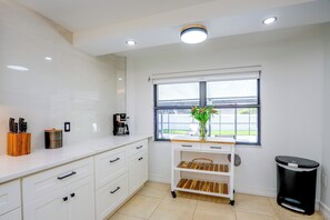 A modern kitchen with white cabinetry, a coffee maker, a knife block, a window with a view, and a trash bin. - Renovated Naples Oasis w/ Pool: 2 Mi to Beach (Naples)