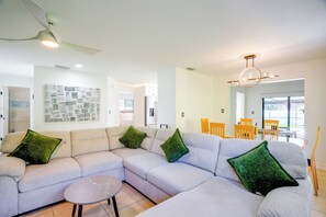Un salon moderne avec un canapé d’angle, une table basse ronde et un coin repas comprenant des chaises en bois et une table en verre.