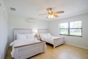 A hotel room with two beds, a ceiling fan, an air conditioning unit, and a window with blinds.