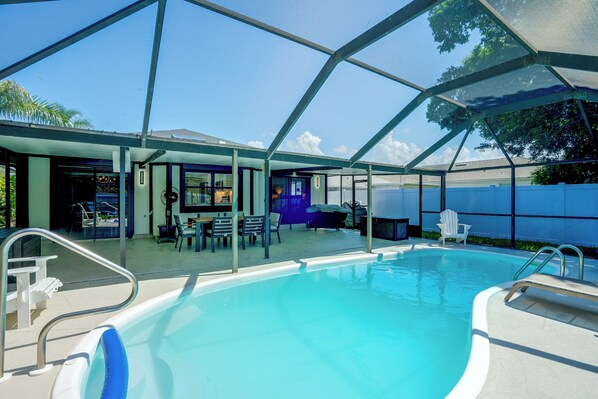 A swimming pool with a covered patio area, outdoor seating, and a view of the sky.