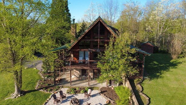 A wooden cabin with a balcony and a deck, surrounded by trees and a well-maintained lawn.