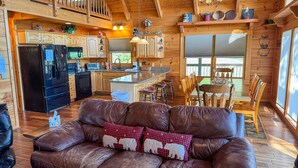 A cozy cabin interior with a dining area, kitchen, and a leather sofa with bear-themed pillows.