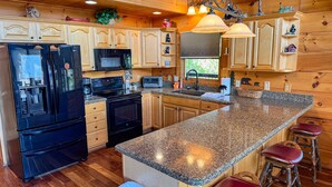 A kitchen with wooden cabinets, a granite countertop, a refrigerator, a stove, a microwave, and a sink.