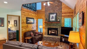 Ein gemütliches Blockhaus-Interieur mit Kamin aus Stein, Holzwänden, einer bequemen Couch und einem Fernseher.