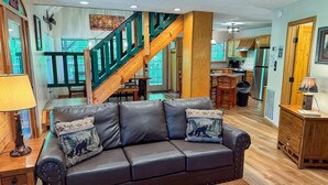 Ein großzügiger Wohnbereich mit Ledersofa, einer Holztreppe und einer Küche im Hintergrund.