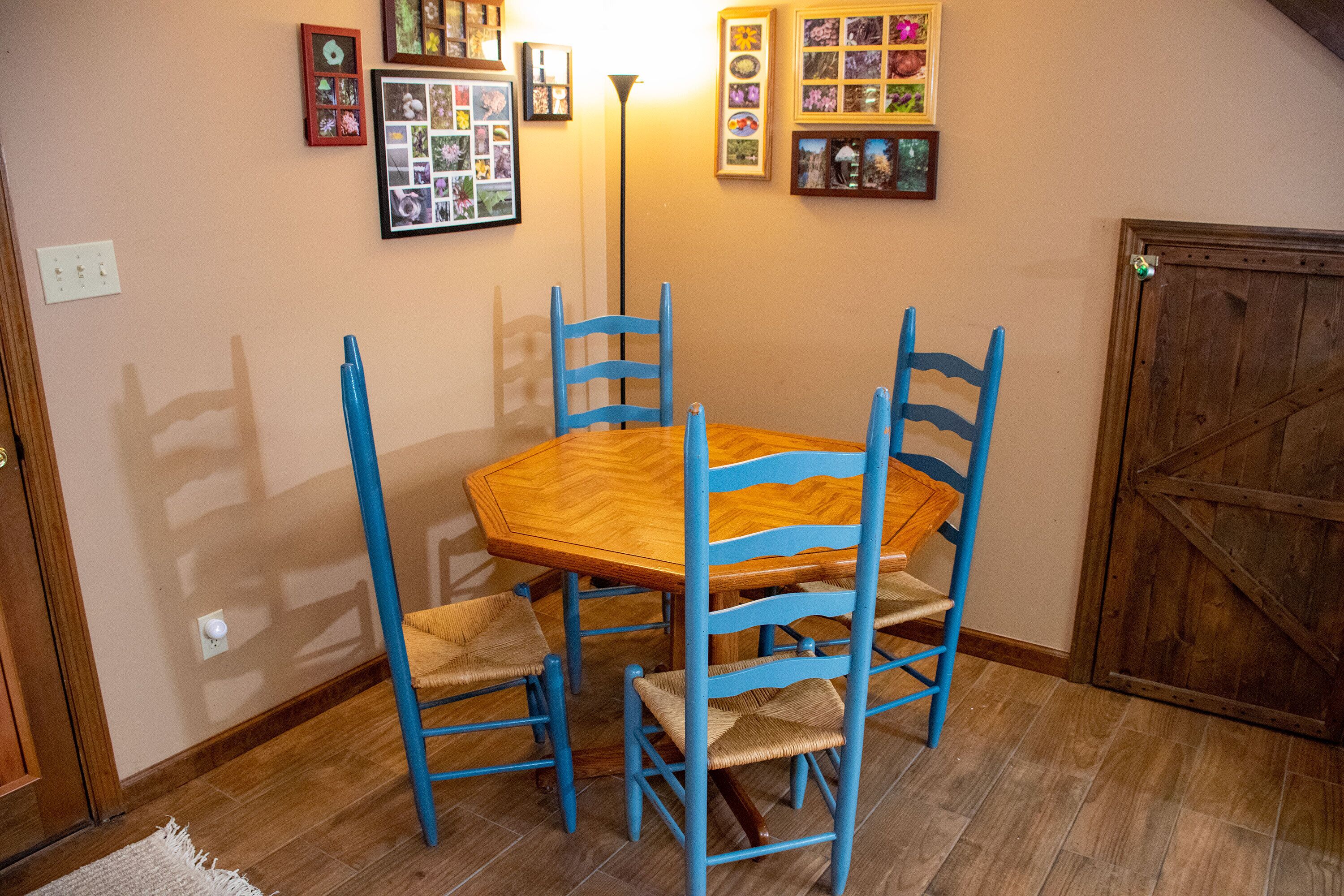 A dining area with a wooden table and blue chairs, a wall with framed photos, and a wooden door.