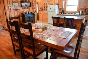 A wooden dining table with chairs, a kitchen area with wooden cabinets, and a refrigerator.