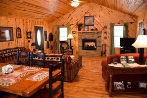 A cozy cabin-style room with a fireplace, wooden walls, a sofa, a dining table, and a television. - Weeks Worth - Cabin in the Smokies (Sevierville)