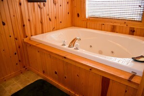 A wooden cabin bathroom with a large bathtub, wooden walls, and a window with blinds. - Weeks Worth - Cabin in the Smokies (Sevierville)