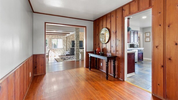 A spacious hallway with wooden paneling, a stone accent wall, and a view into a kitchen area.