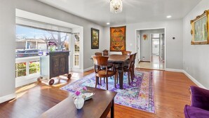 A spacious dining area with a wooden table and chairs, a chandelier, and a large window with a view of the outside.