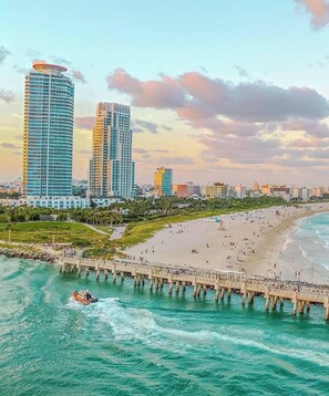 A coastal cityscape with a beach, a pier, and modern high-rise buildings.