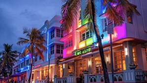 A brightly lit hotel with a neon sign, palm trees, and a street view. - Directly on the beach with Free beach lounges.  Best location in South Beach! (Miami Beach)