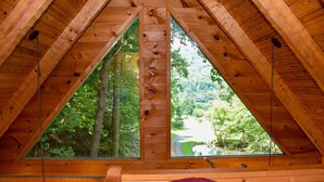 A wooden cabin with a triangular roof and two large windows offering a view of a forested area. - Sweet Serenity - Easy to Access Cabin By A Small Mountain Stream in Wears Valley (Sevierville)