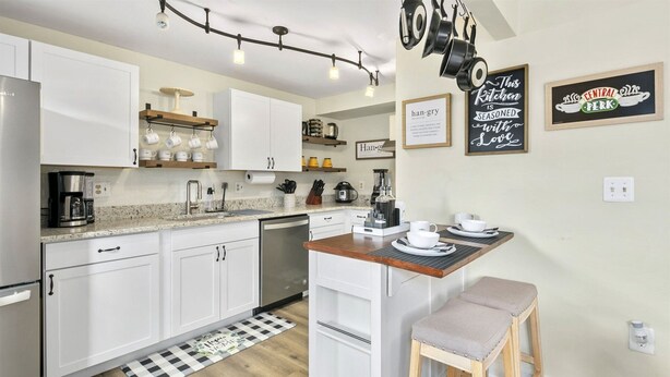 A modern kitchen with white cabinets, a wooden island, and a coffee station. There are wall decorations and a checkered mat at the entrance. - QuincyHideaway: Quaint Townhome Near DC (Sterling)