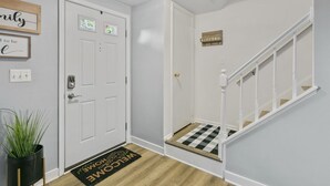 A clean, modern hallway with a white door, a welcome mat, and a staircase with white railings. - QuincyHideaway: Quaint Townhome Near DC (Sterling)
