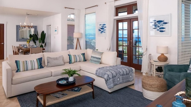 Uma sala de estar moderna com um sofá bege, uma mesa de centro e vista para o mar através de grandes janelas.