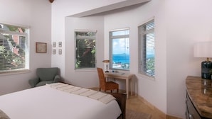 Quarto com cama, escrivaninha, cadeira e vista para o mar.
