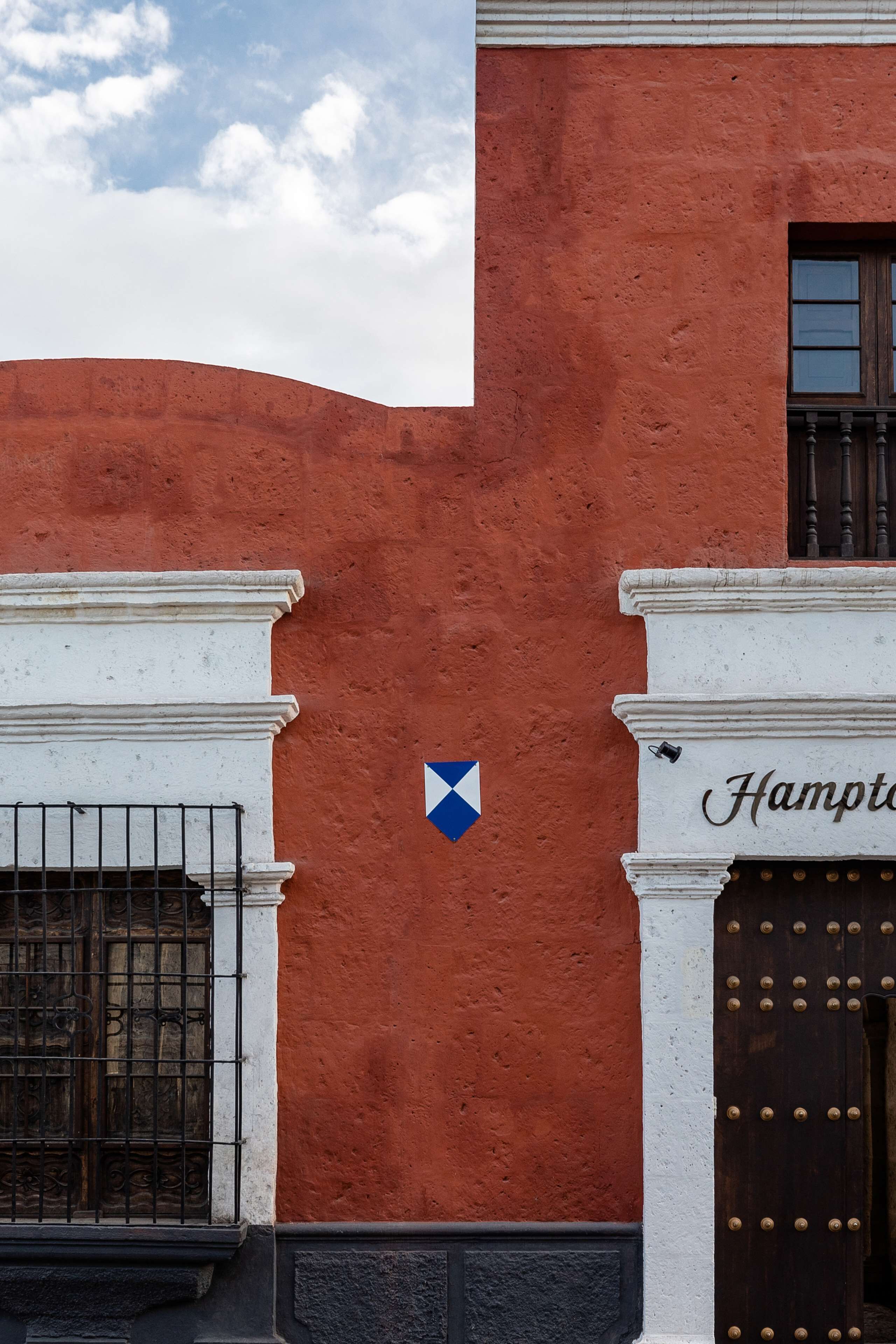 Fachada de un edificio con pared roja, columnas blancas, un letrero azul en forma de diamante y una puerta con una placa que dice "Hampton".