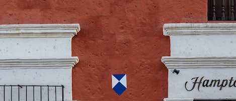 Fachada de un edificio con pared roja, columnas blancas, un letrero azul en forma de diamante y una puerta con una placa que dice "Hampton".