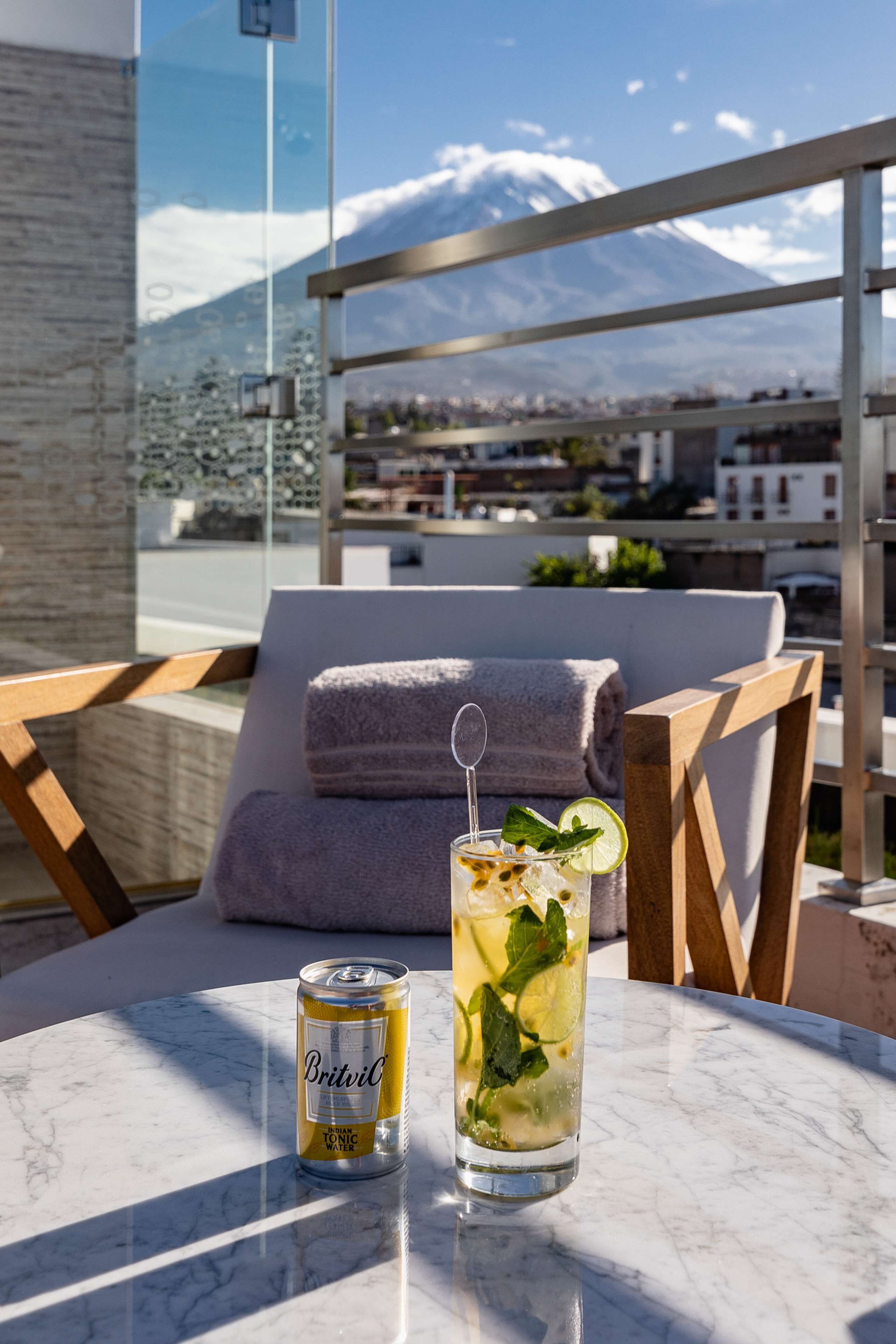 A can of Britvic tonic water and a glass of iced drink with mint on a marble table.