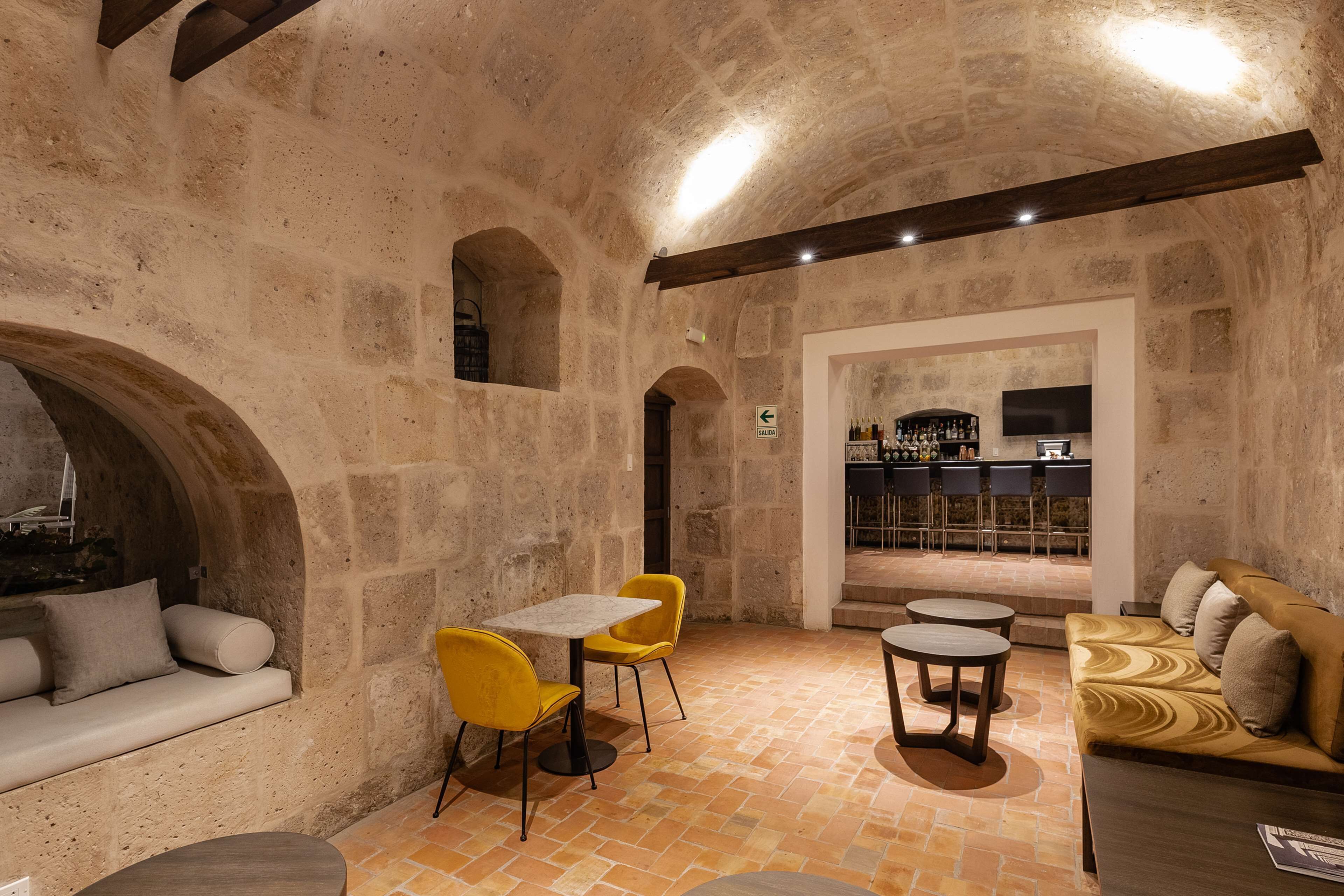 Un intérieur aux murs de pierre, avec un coin bar, des chaises jaunes et un canapé.