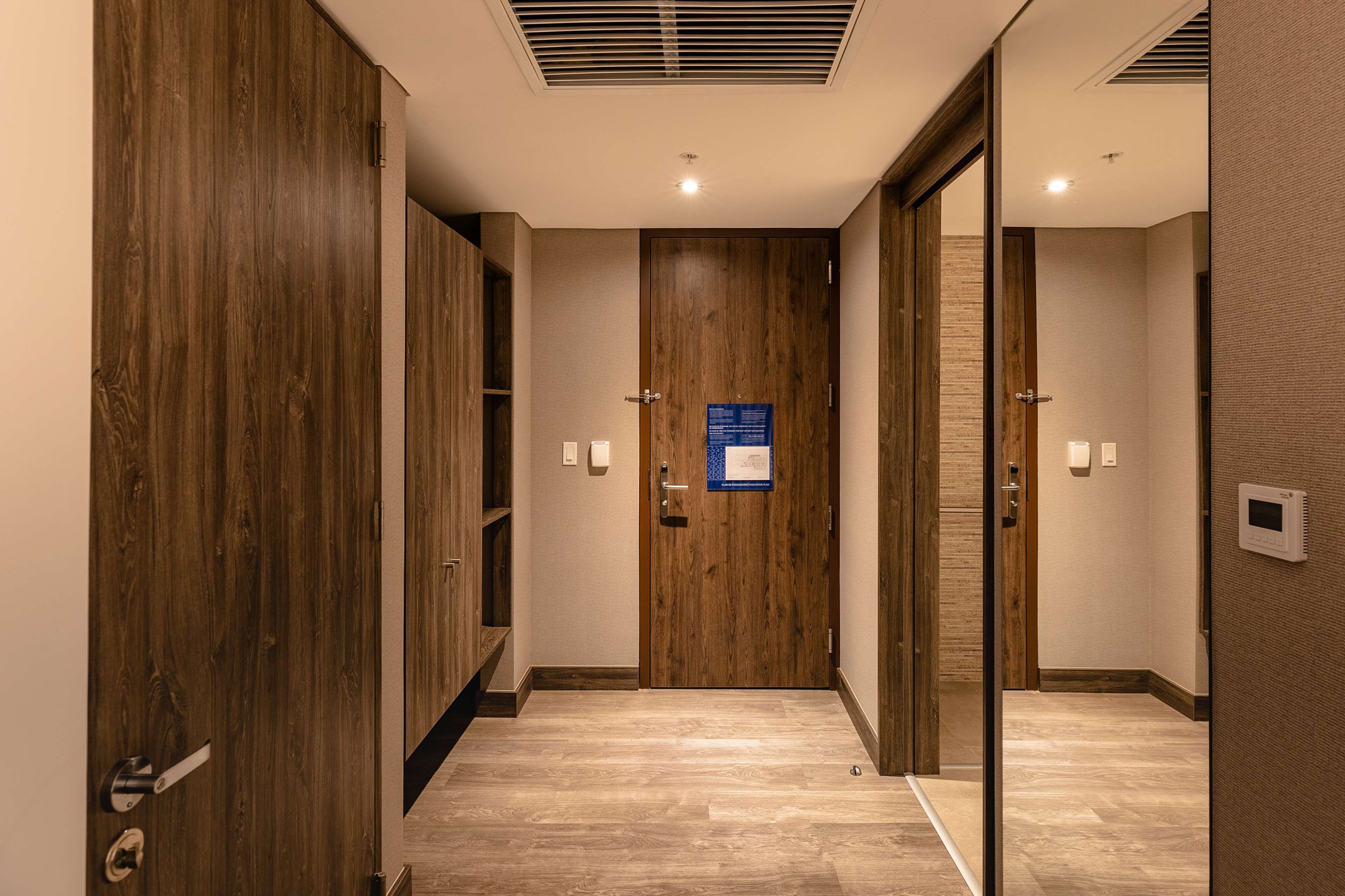 A hotel hallway with wooden doors, a blue sign, and a thermostat on the wall.