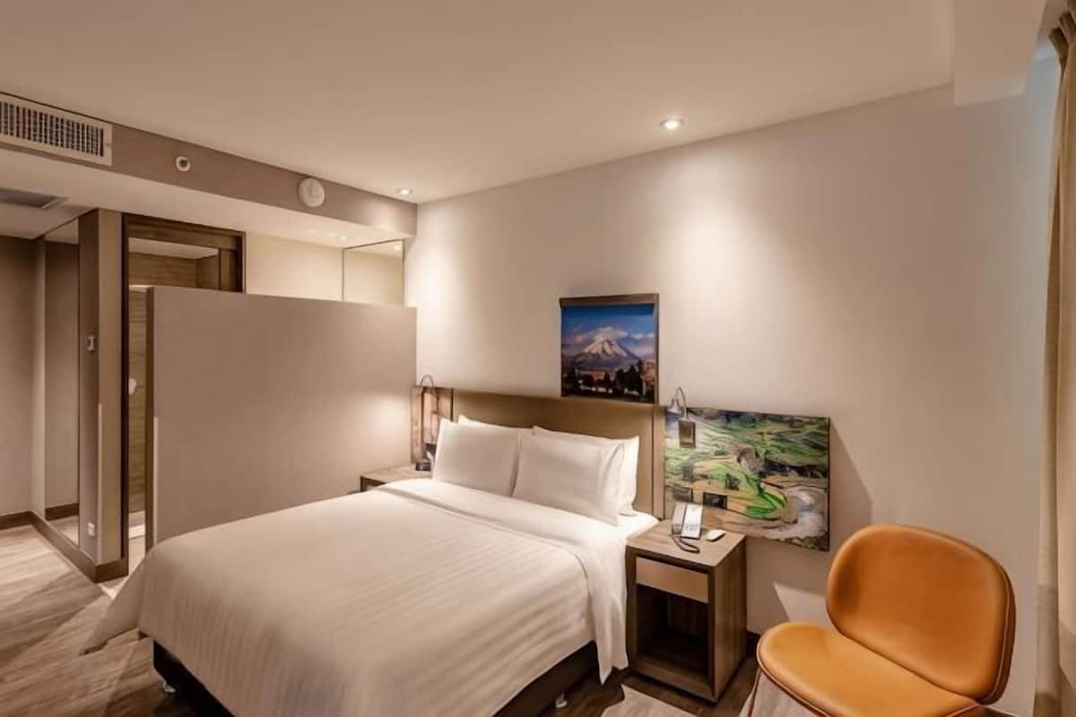 Una habitación de hotel con cama, mesita de noche, lámpara y una silla.