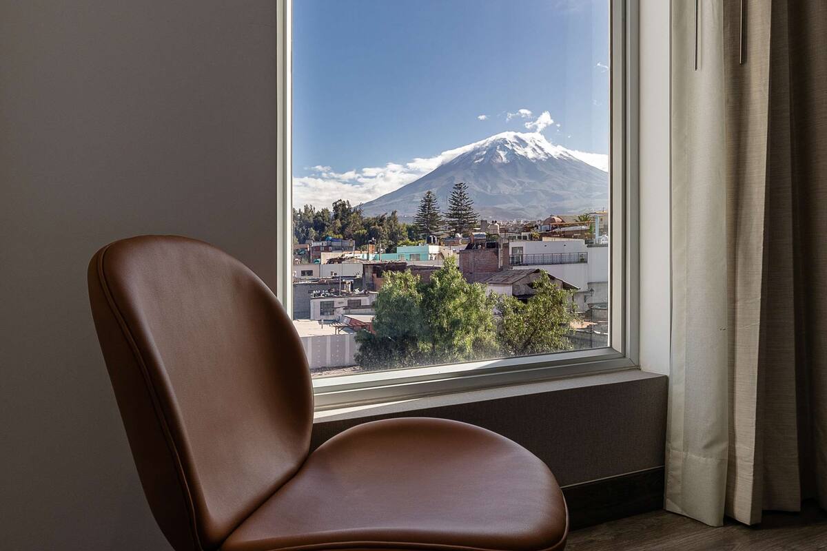 A room with a large window, a brown chair, and a view of a mountain.