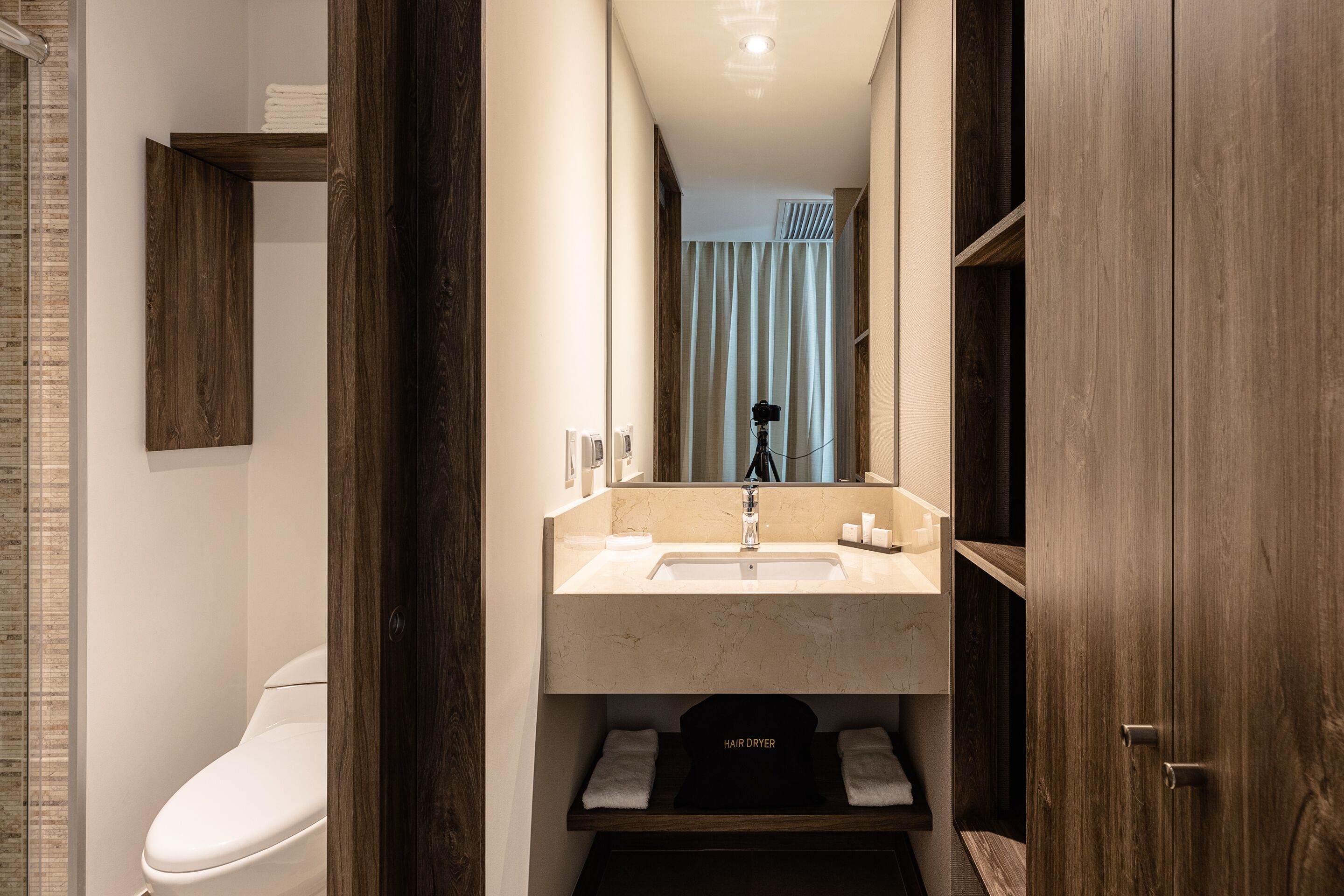 Un baño moderno con inodoro blanco, lavabo con espejo arriba y zona de ducha visible a través de una cortina.