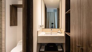Un baño moderno con inodoro blanco, lavabo con espejo arriba y zona de ducha visible a través de una cortina.