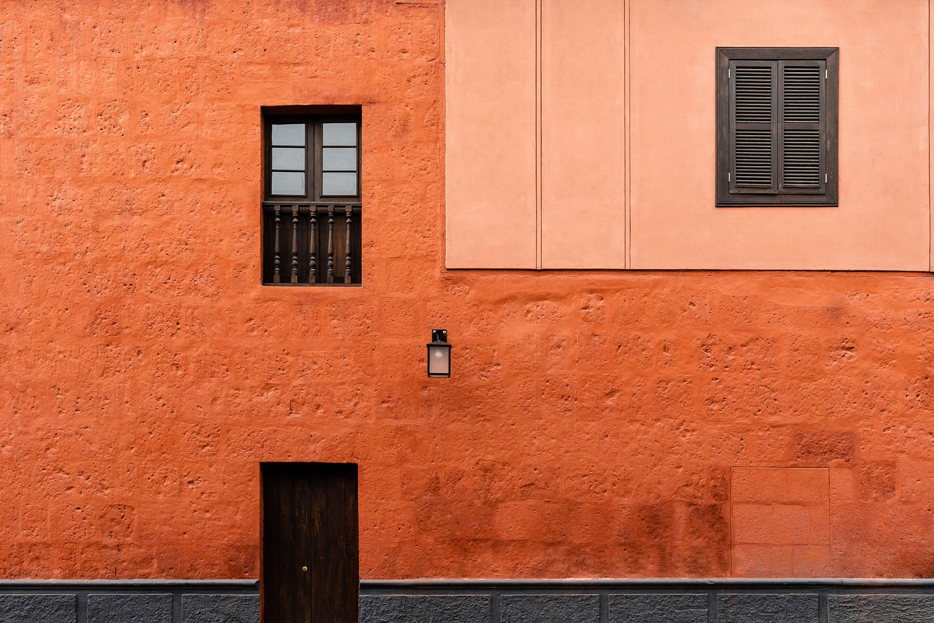 Un bâtiment doté d ’une façade orange à texture, d’une petite fenêtre ornée d’une grille métallique et d’une porte.