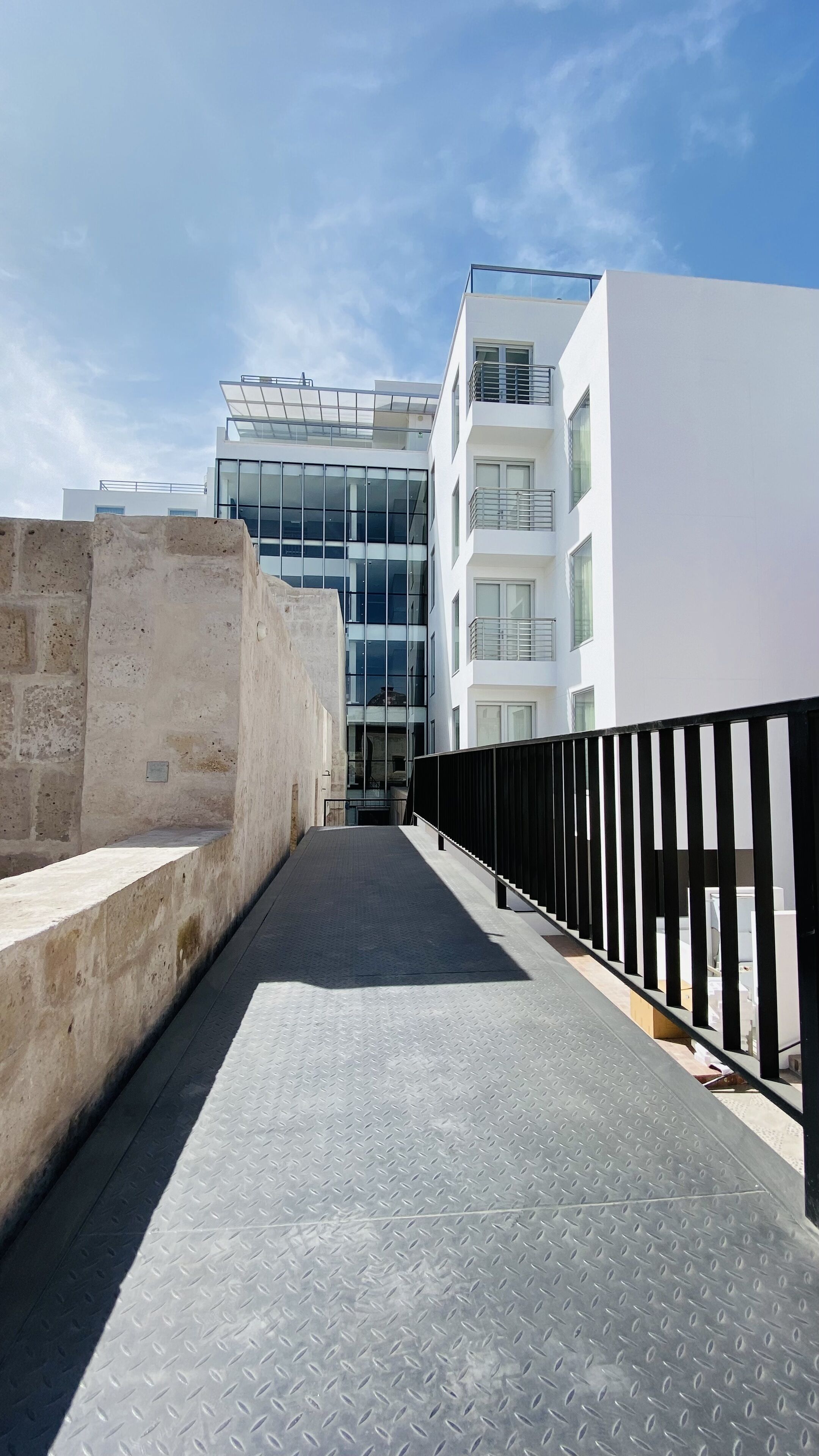 A modern building with large windows and a balcony, a narrow pathway, and a metal fence.