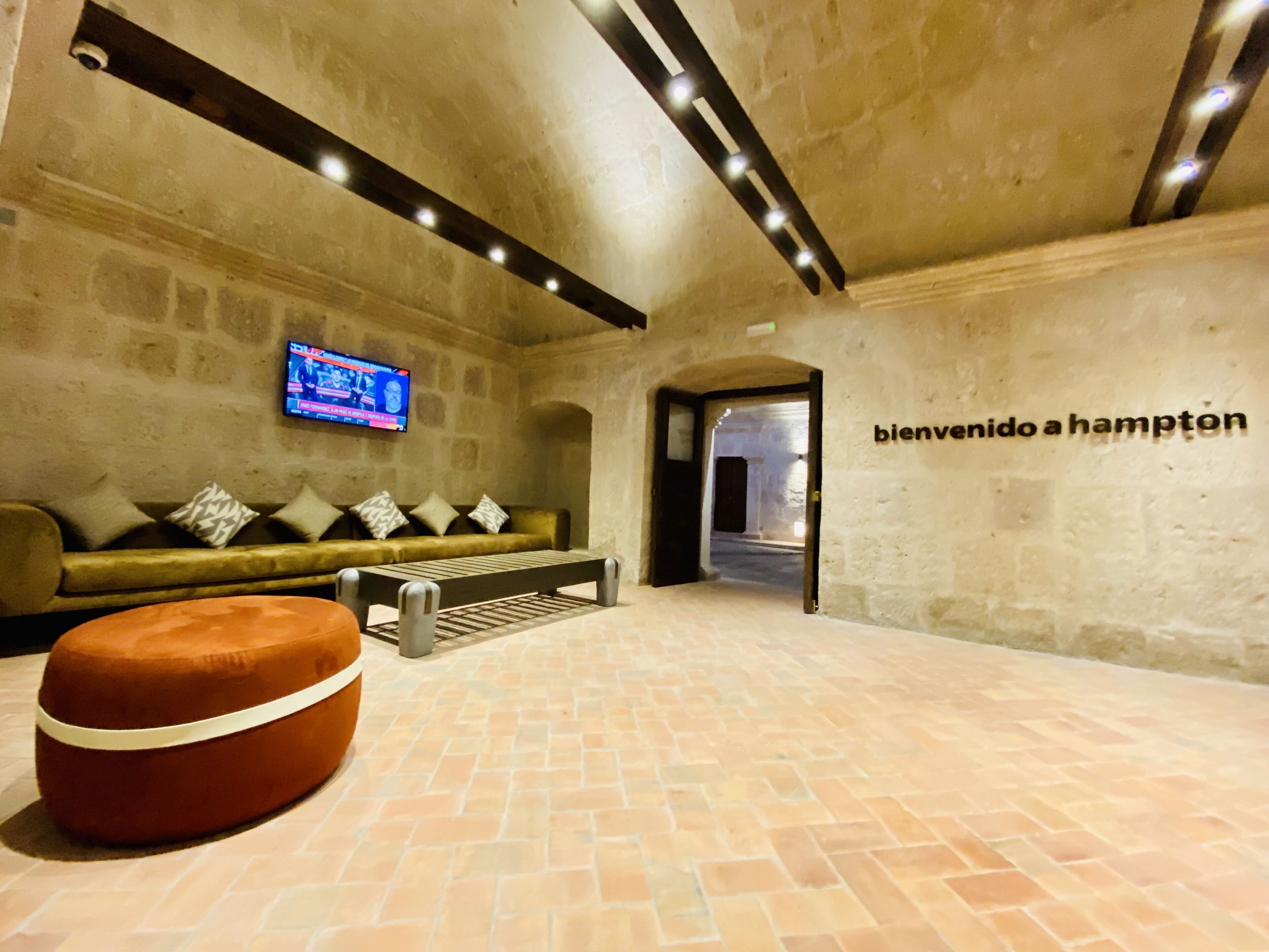 A lobby with a stone wall, a sofa with patterned cushions, a television, and a sign reading "bienvenido a Hampton".